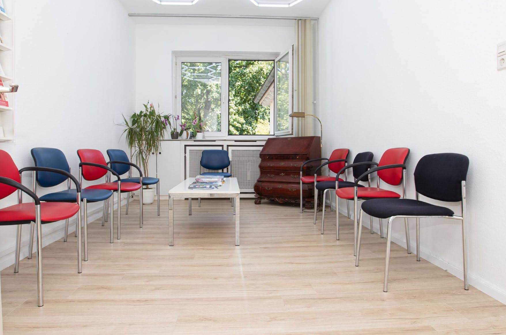 Das Wartezimmer der Praxis mit Stühlen, Pflanzen und Blick auf grüne Bäume